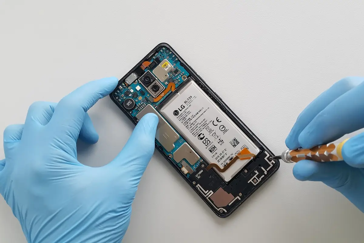 Técnico de luvas azuis trocando a bateria do celular na bancada